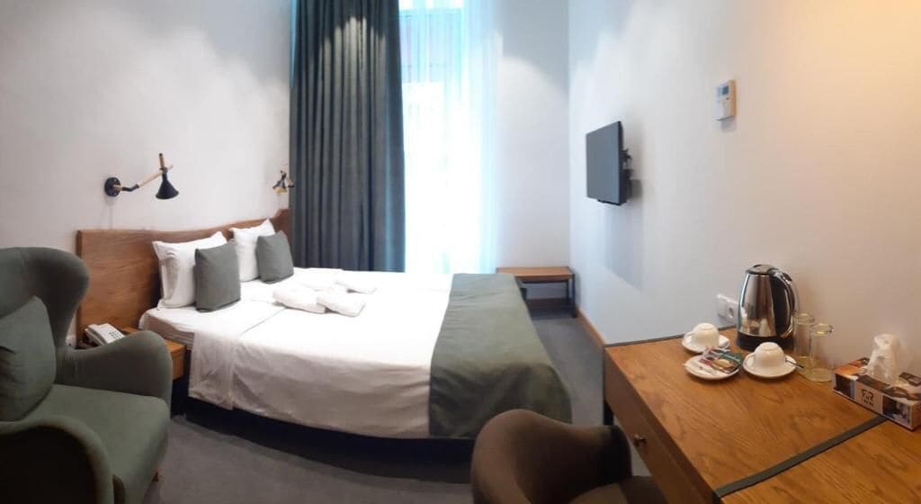 A hotel room with a bed, a desk with a kettle, cups, and a small table.