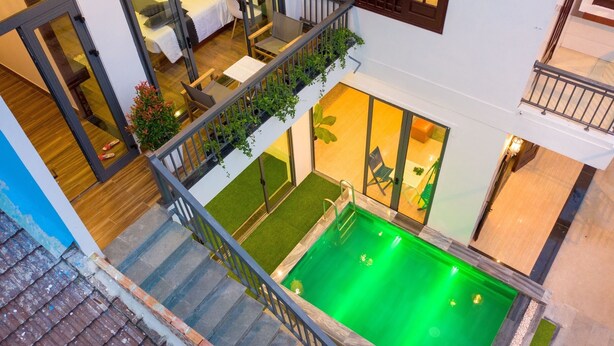 Um edifício residencial com vários andares, uma piscina no terraço, uma varanda com plantas e uma área de refeições com mesa e cadeiras.