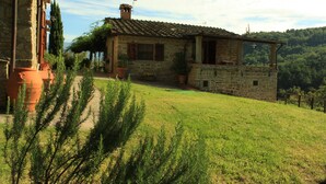 Una casa de piedra con tejado de tejas, rodeada de césped y plantas en macetas.