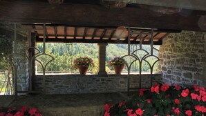 Un edificio de piedra con balcón de madera, plantas en macetas y vistas al verdor.
