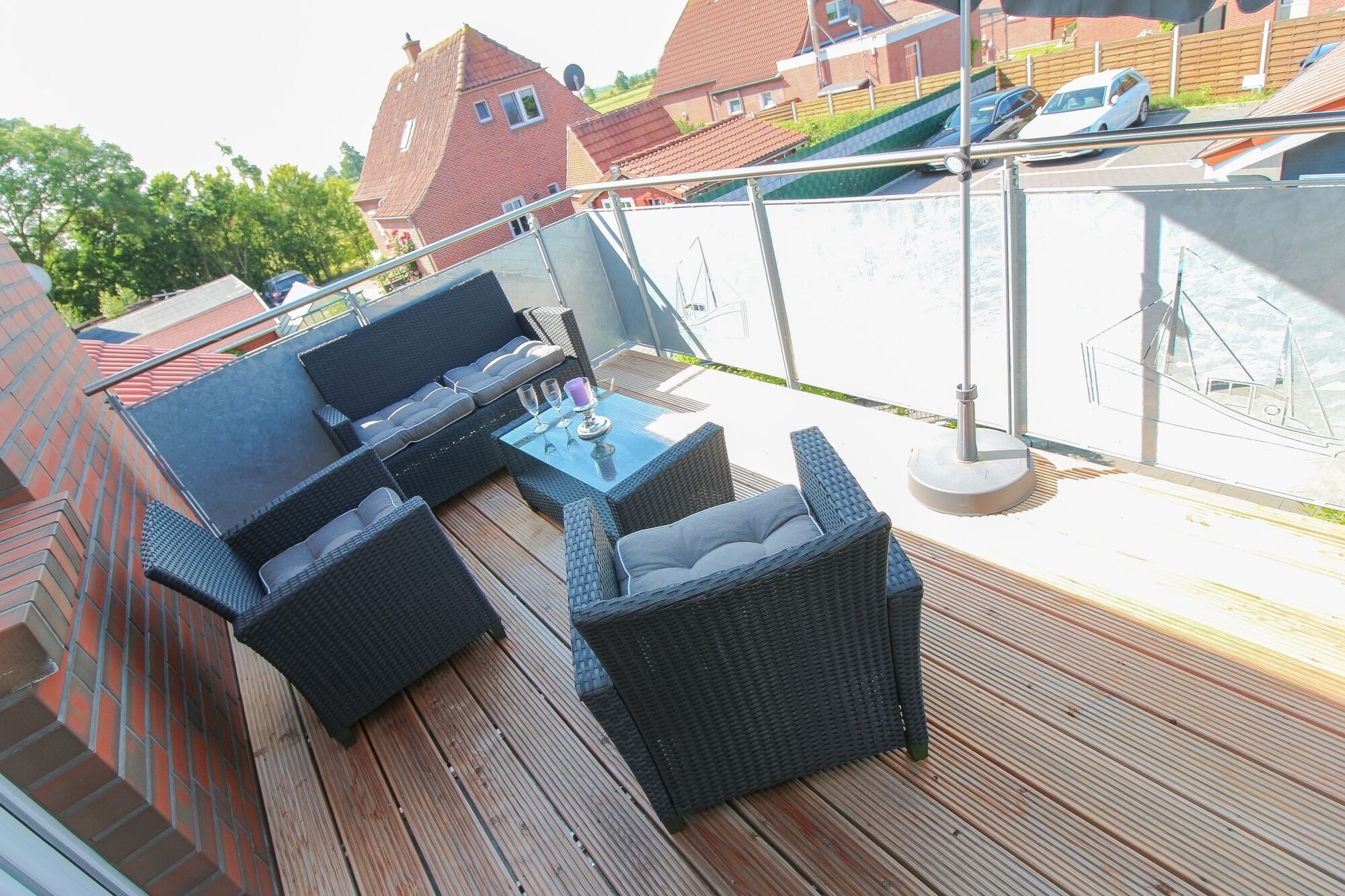 An outdoor deck with wicker furniture, a glass table, and a view of a residential area.