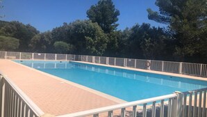 Piscina retangular com cerca branca ao redor, com árvores e céu claro ao fundo.