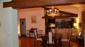 Uma sala de jantar com mesa e cadeiras de madeira, um lustre e uma cozinha ao fundo.