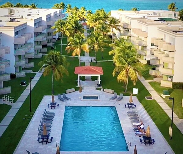 Ett semesterhotell med en central pool, omgivet av solstolar och palmer.