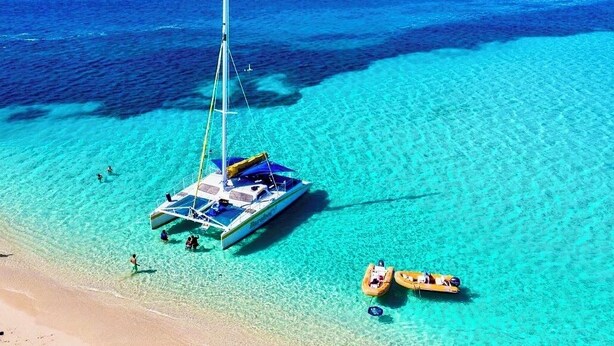 Un mar azul y transparente con un velero anclado cerca de la costa.