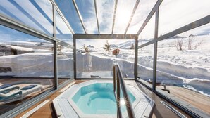 Un jacuzzi con paredes de vidrio que ofrece vistas a un paisaje nevado y montañas.
