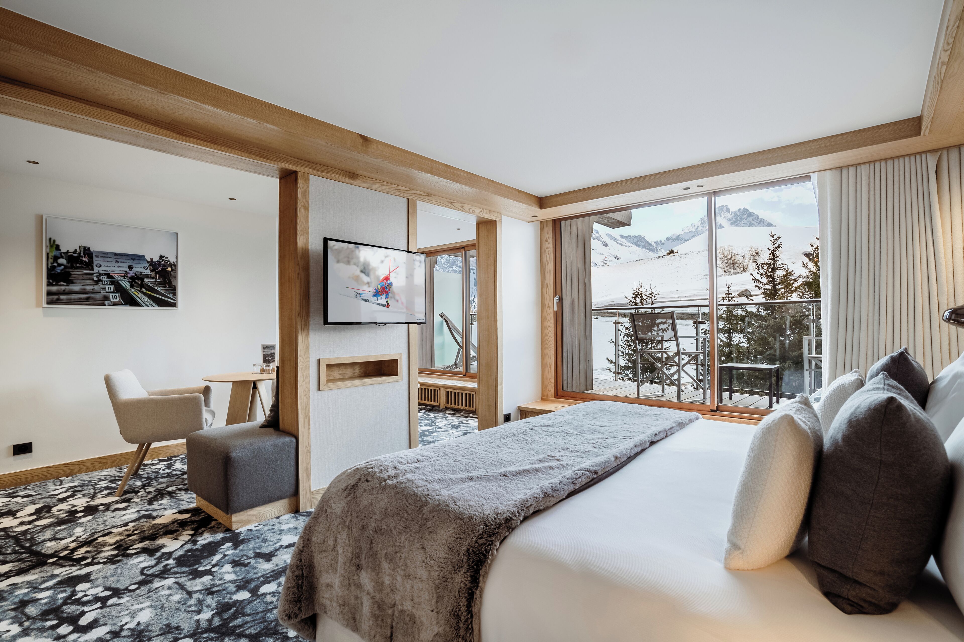 A modern hotel room with a large bed, a TV, a desk, and a window with a mountain view.