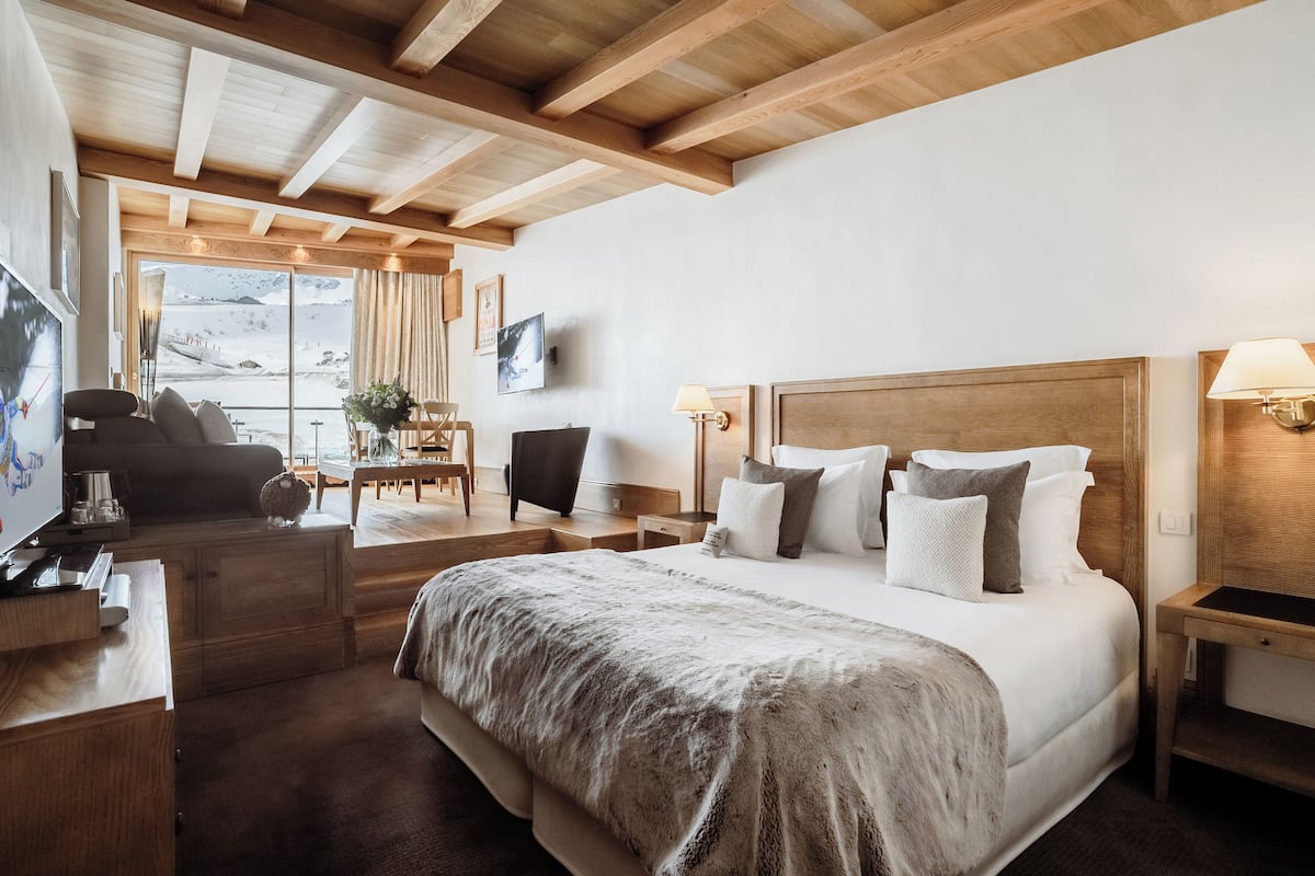 Une chambre avec un grand lit, une tête de lit en bois, des tables de chevet, une télévision et une vue sur un paysage enneigé par la fenêtre.