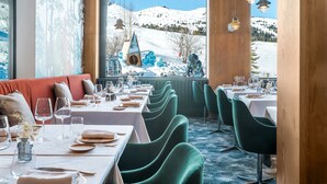 Un restaurante con mesas dispuestas para comer, vistas a montañas nevadas y un interior acogedor con detalles de madera y sillas verdes.