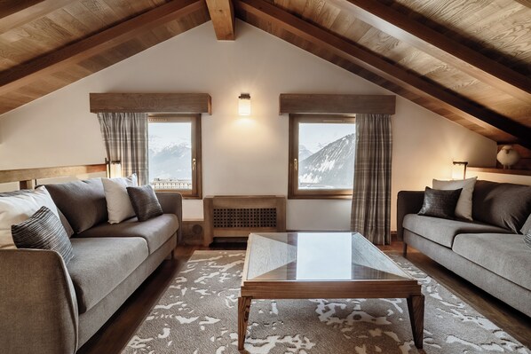 A cozy loft bedroom with a high ceiling, two sofas, a glass coffee table, and mountain views through large windows.