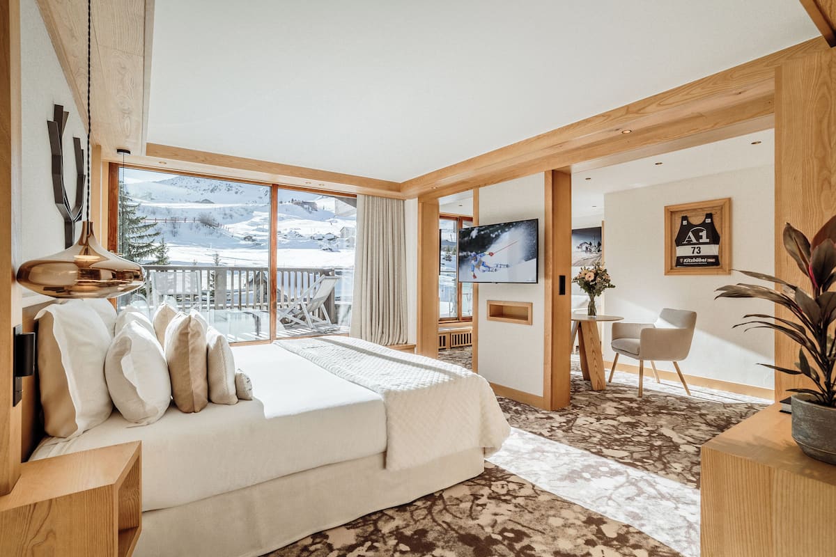 Une chambre d’hôtel moderne avec un grand lit, une télévision, un bureau et une vue sur une montagne enneigée.
