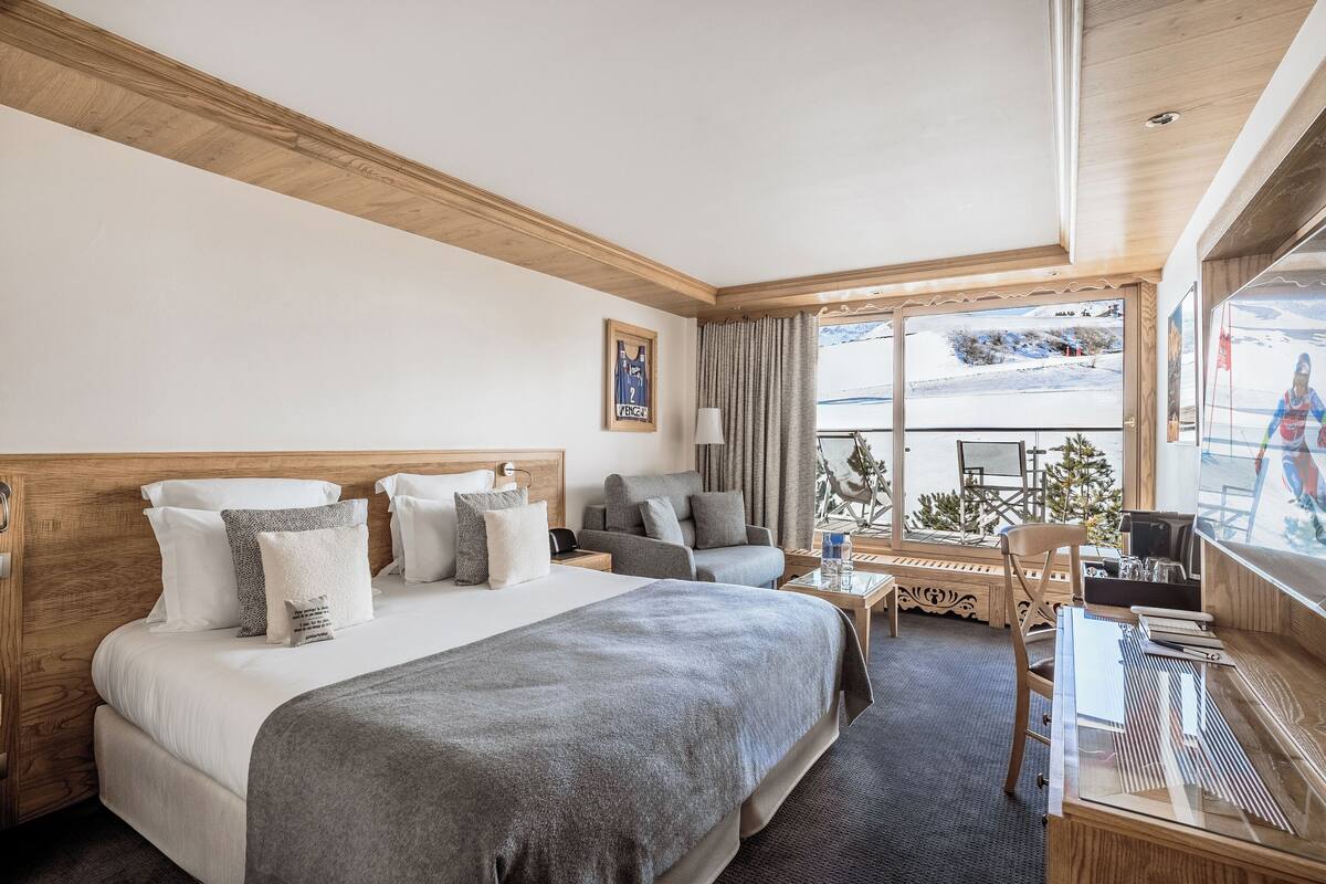 Une chambre d’hôtel avec un grand lit, un bureau, une chaise et une fenêtre donnant sur un paysage enneigé.