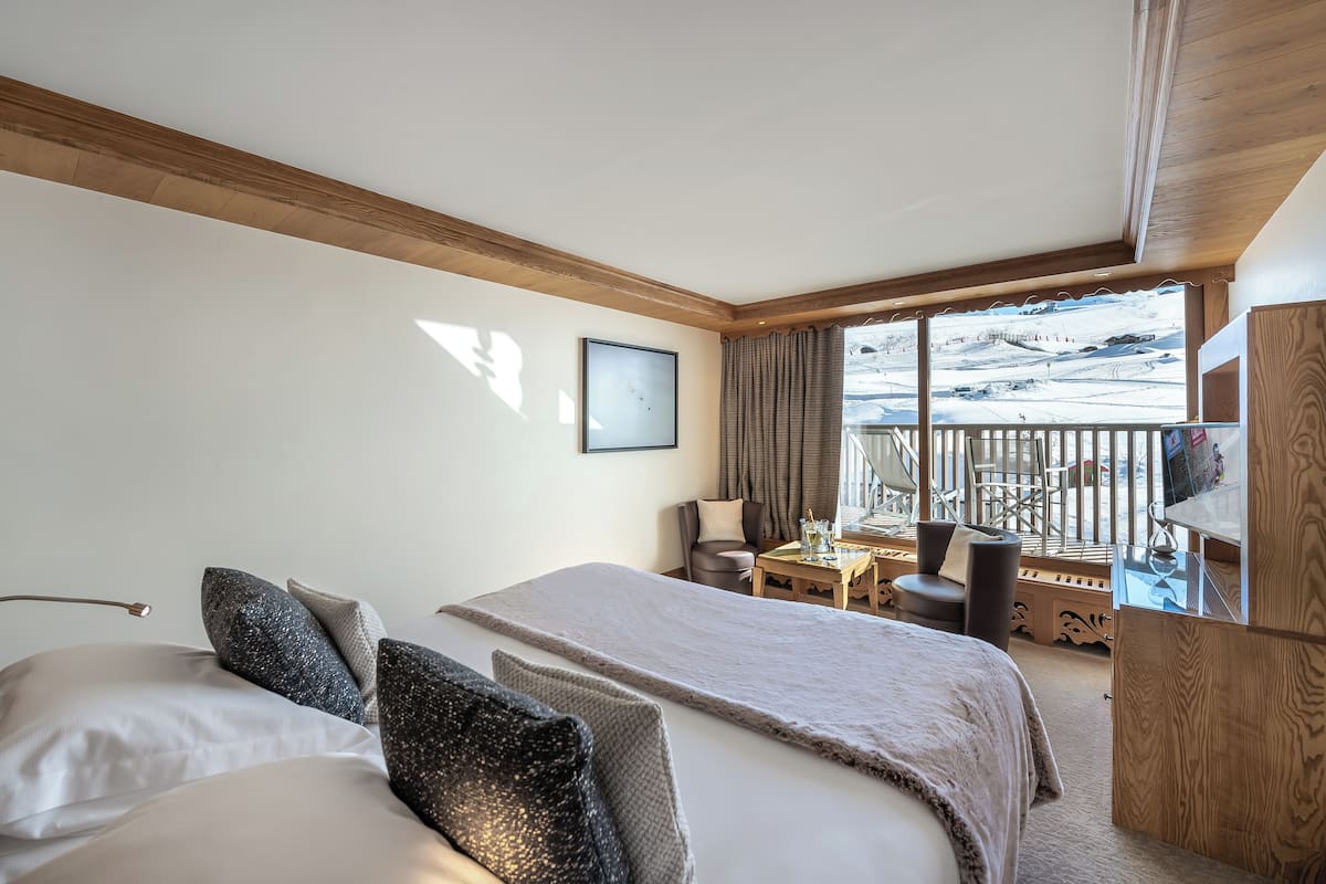 Une chambre d’hôtel avec un lit, un bureau et un balcon donnant sur les pistes de ski.