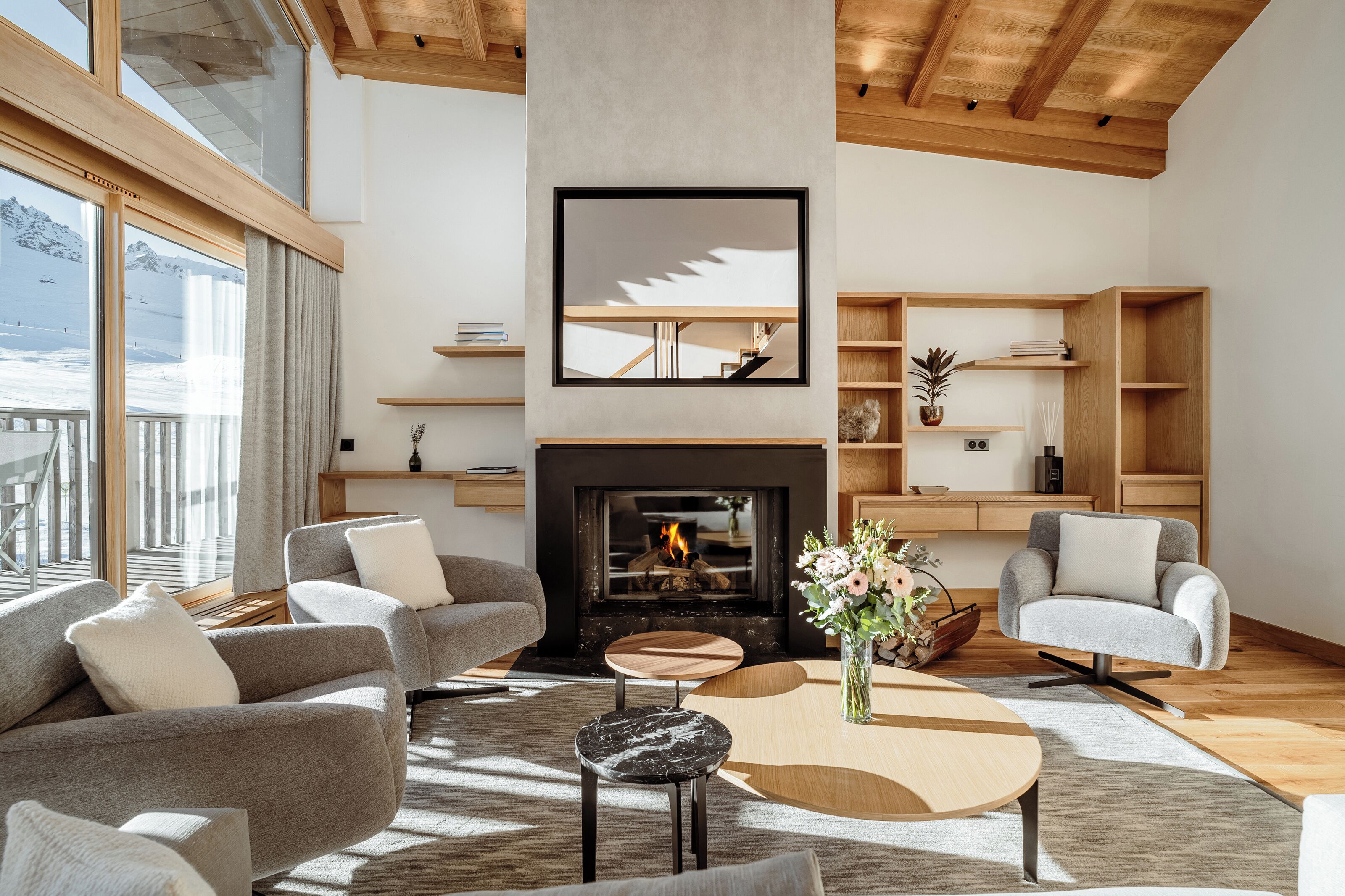 A modern living room with a fireplace, wooden shelves, and a large window overlooking a snowy landscape.
