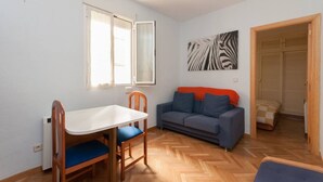 A compact living space with a dining table and chairs, a sofa, and a herringbone-patterned wooden floor. - Beautiful apartment (Madrid)