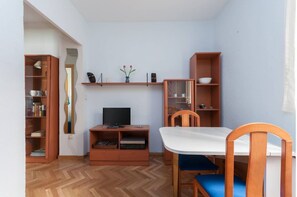 A compact living space with a dining table, chairs, a TV, and built-in shelving with books and decorative items. - Beautiful apartment (Madrid)