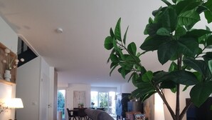 Un salon spacieux avec un canapé gris, un coin repas à l’arrière-plan et une grande plante dans un panier en osier.