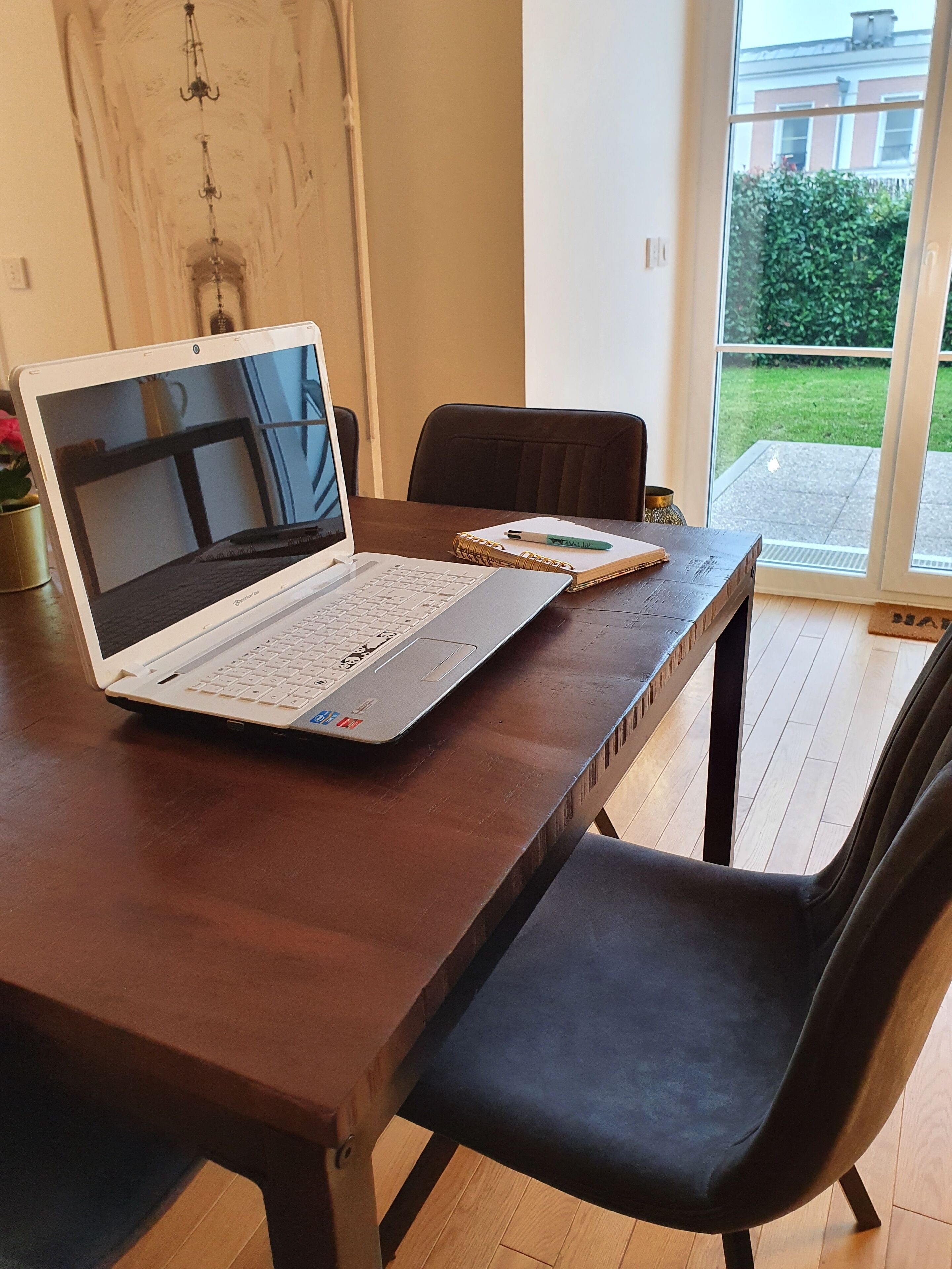 Un portatile su un tavolo di legno, con un quaderno e una penna accanto.