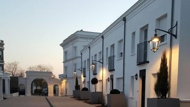 Une cour pavée bordée de bâtiments blancs, chacun doté d’un balcon et d’un lampadaire.