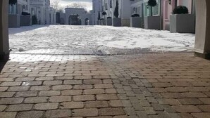 Une rue pavée bordée de bâtiments des deux côtés, vue à travers une arche.