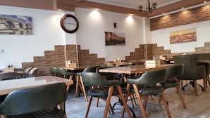 A modern dining area with wooden tables and chairs, a large wall clock, and artwork.
