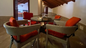 A dining area with wicker chairs and a glass table, wooden beams on the ceiling, and a door leading to another room.
