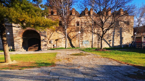 A historic stone building with a large arched entrance, surrounded by a grassy area and trees.