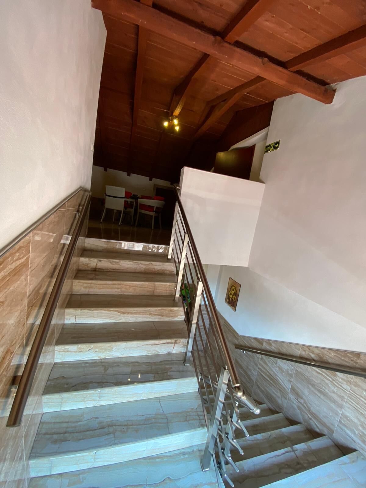 A staircase with marble steps and metal railings, leading to a dining area with tables and chairs.