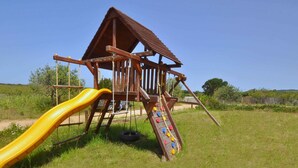 A wooden play structure with a slide and climbing wall in a grassy field. - Residence a Badesi ID 3369 (Trinita d'Agultu e Vignola)