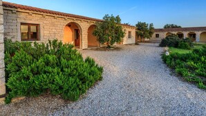 A courtyard with stone buildings, gravel paths, and green shrubs. - Residence a Badesi ID 3369 (Trinita d'Agultu e Vignola)