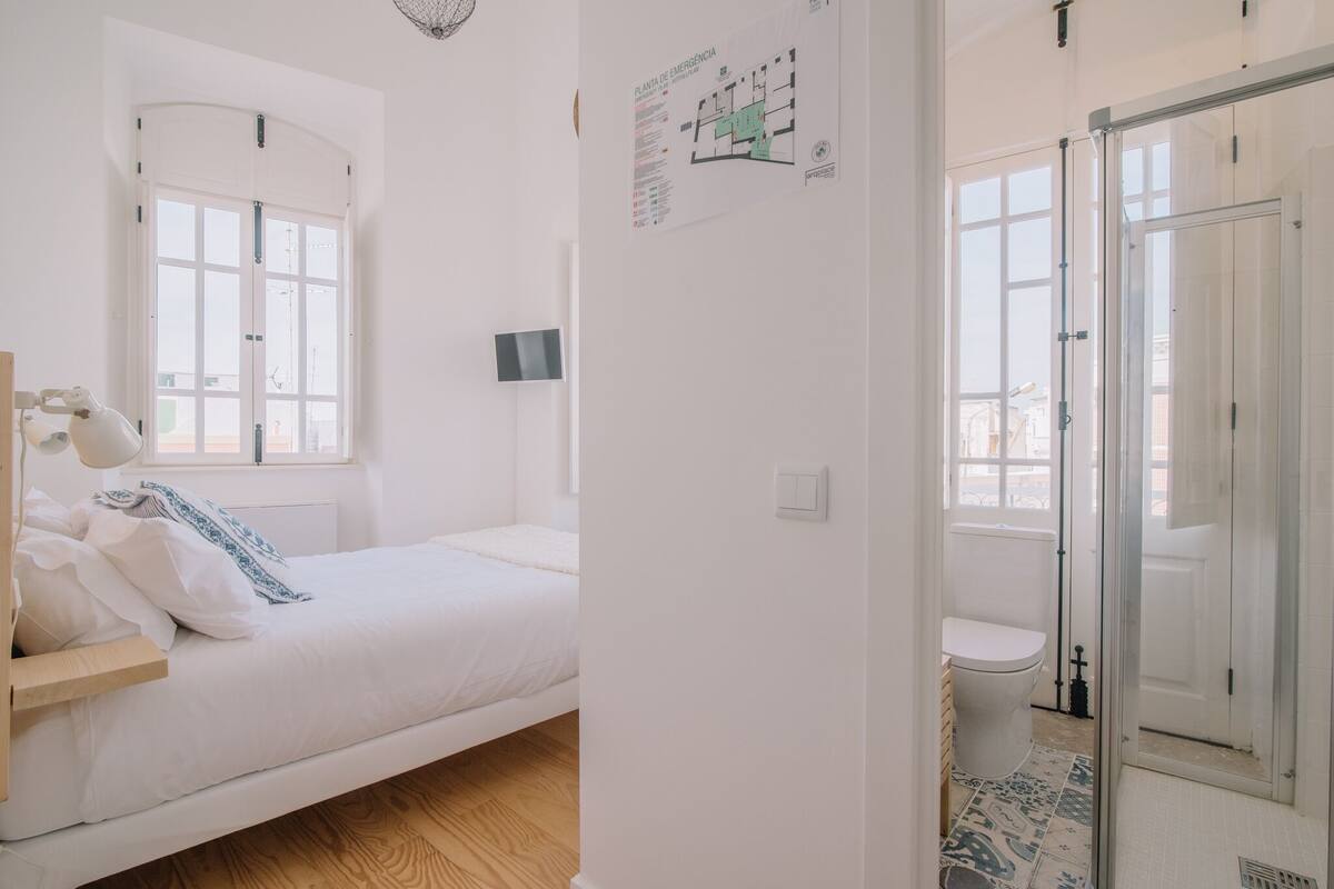 Une chambre à coucher comprenant un lit, une table de chevet, une fenêtre et une salle de bain avec des toilettes et une douche.
