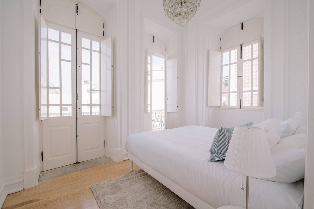 Une chambre à coucher avec un grand lit, une lampe de chevet et une vue sur l’extérieur par une fenêtre.