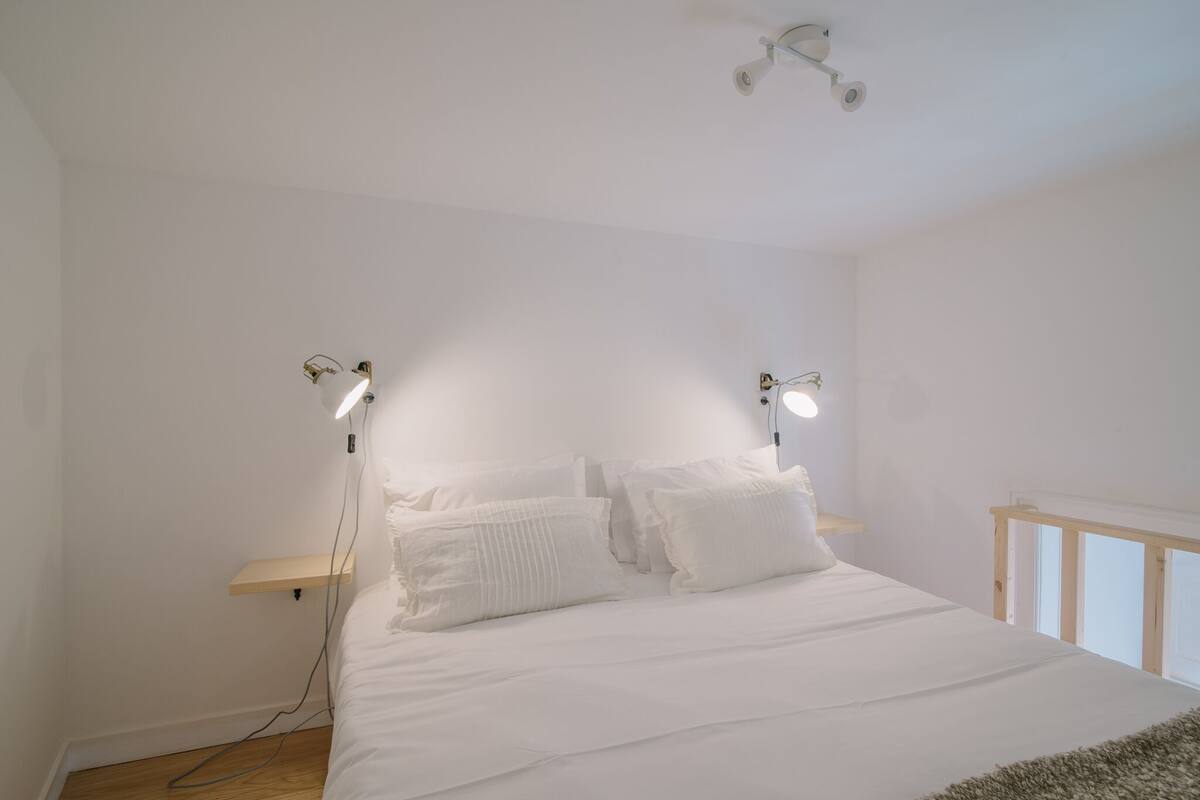 Une chambre à coucher au style minimaliste, avec un grand lit, deux tables de chevet et un luminaire suspendu au plafond.