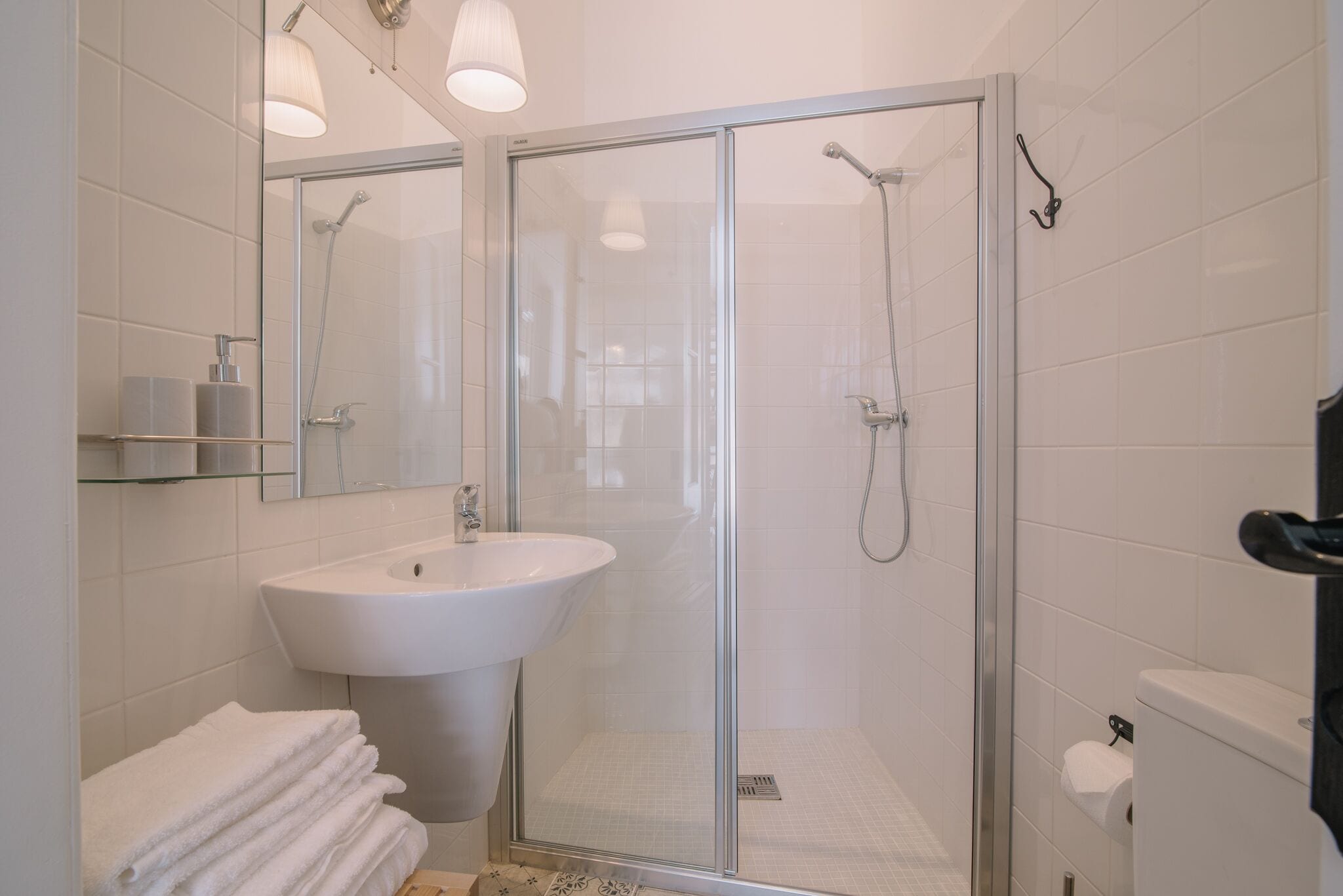 A modern bathroom with a glass-enclosed shower, a white sink, and a stack of white towels.