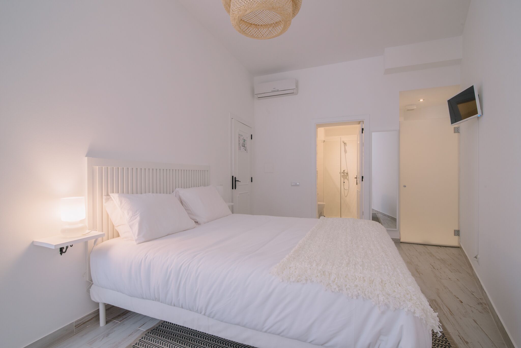 Ein schlicht eingerichtetes Schlafzimmer mit Bett, Nachttischlampe und einem an der Wand befestigten Fernseher.