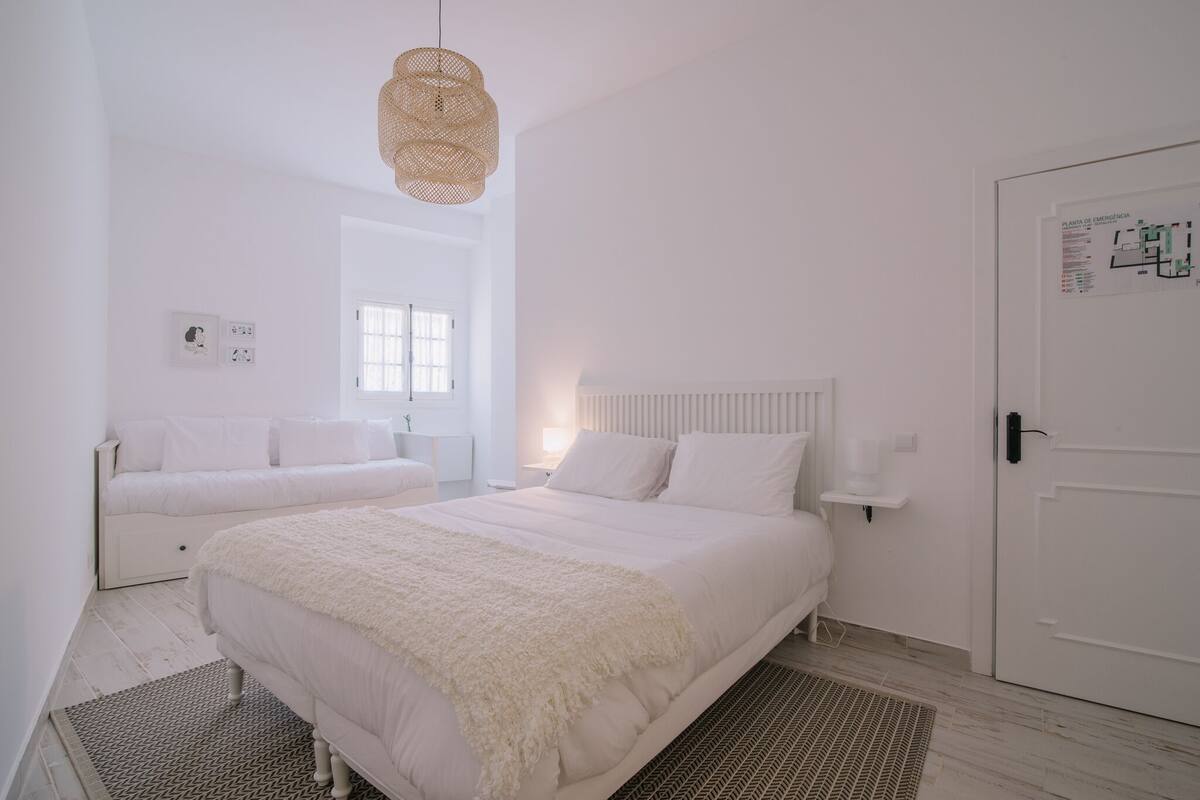 Une chambre à coucher au style minimaliste, avec deux lits, une grande fenêtre et une porte sur laquelle figurent les consignes de sécurité en cas d’urgence.