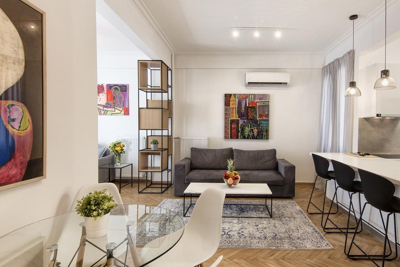 A modern living room with a grey sofa, a glass coffee table, and a dining area with a white table and black chairs.