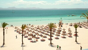 Una playa con numerosas sombrillas y palmeras, una torre de salvavidas y una vista despejada del mar.