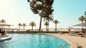 Una piscina con agua cristalina azul, rodeada de palmeras y zonas de estar al aire libre.