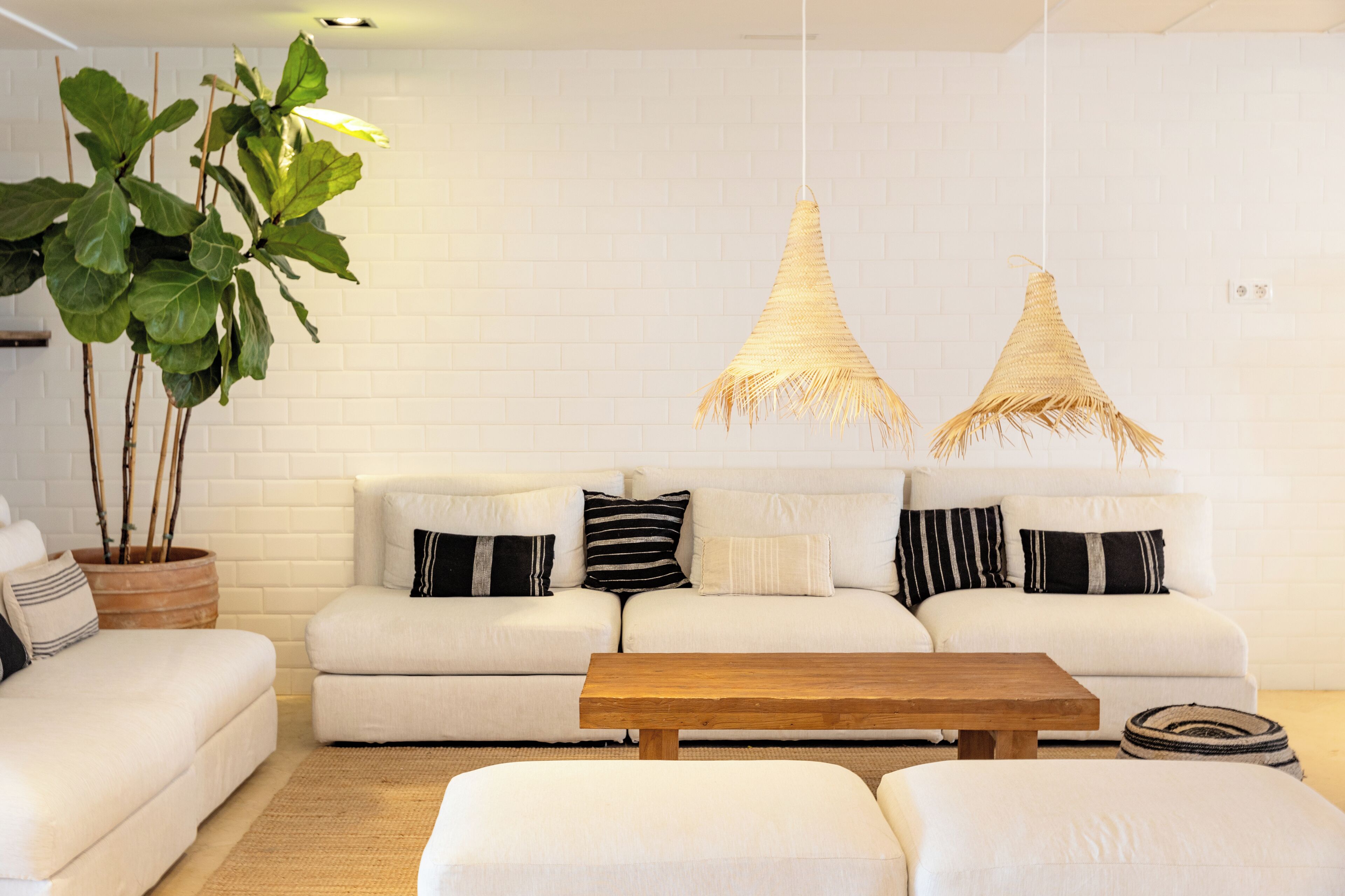 Een moderne woonkamer met een witte baksteenmuur, een witte zithoek, twee hanglampen van rotan en een houten salontafel.