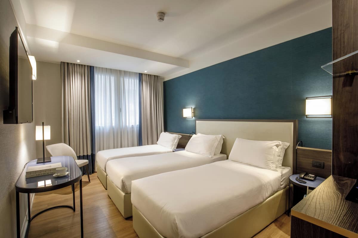 A hotel room with two beds, a desk with a lamp, and a small table with a phone.