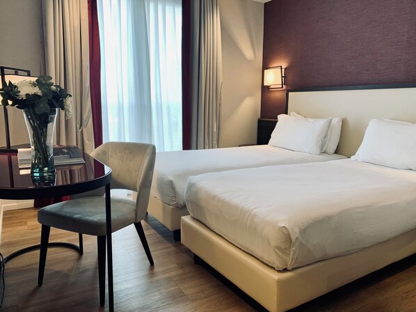 Une chambre d’hôtel avec deux lits, un bureau avec une chaise et un vase de fleurs.