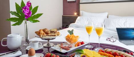 Hotelkamer met ontbijtbuffet, een laptop op het bed en een schilderij aan de muur.