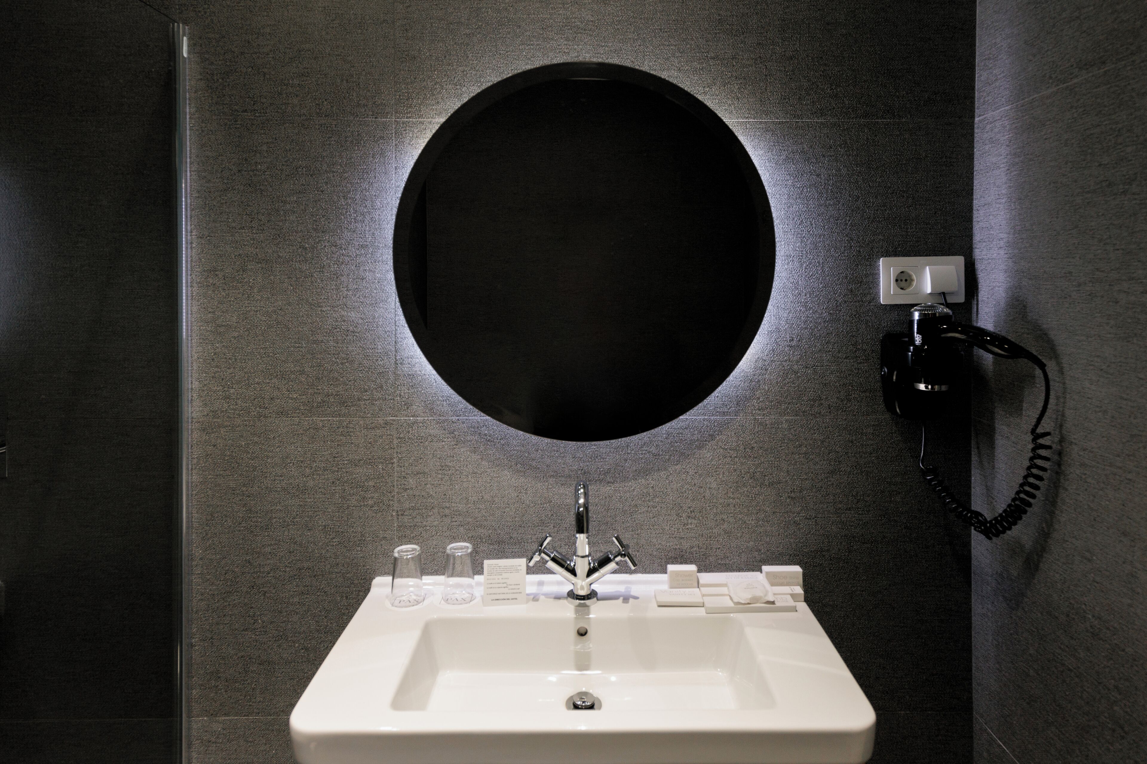A modern bathroom with a round mirror, a white sink, and a telephone mounted on the wall.