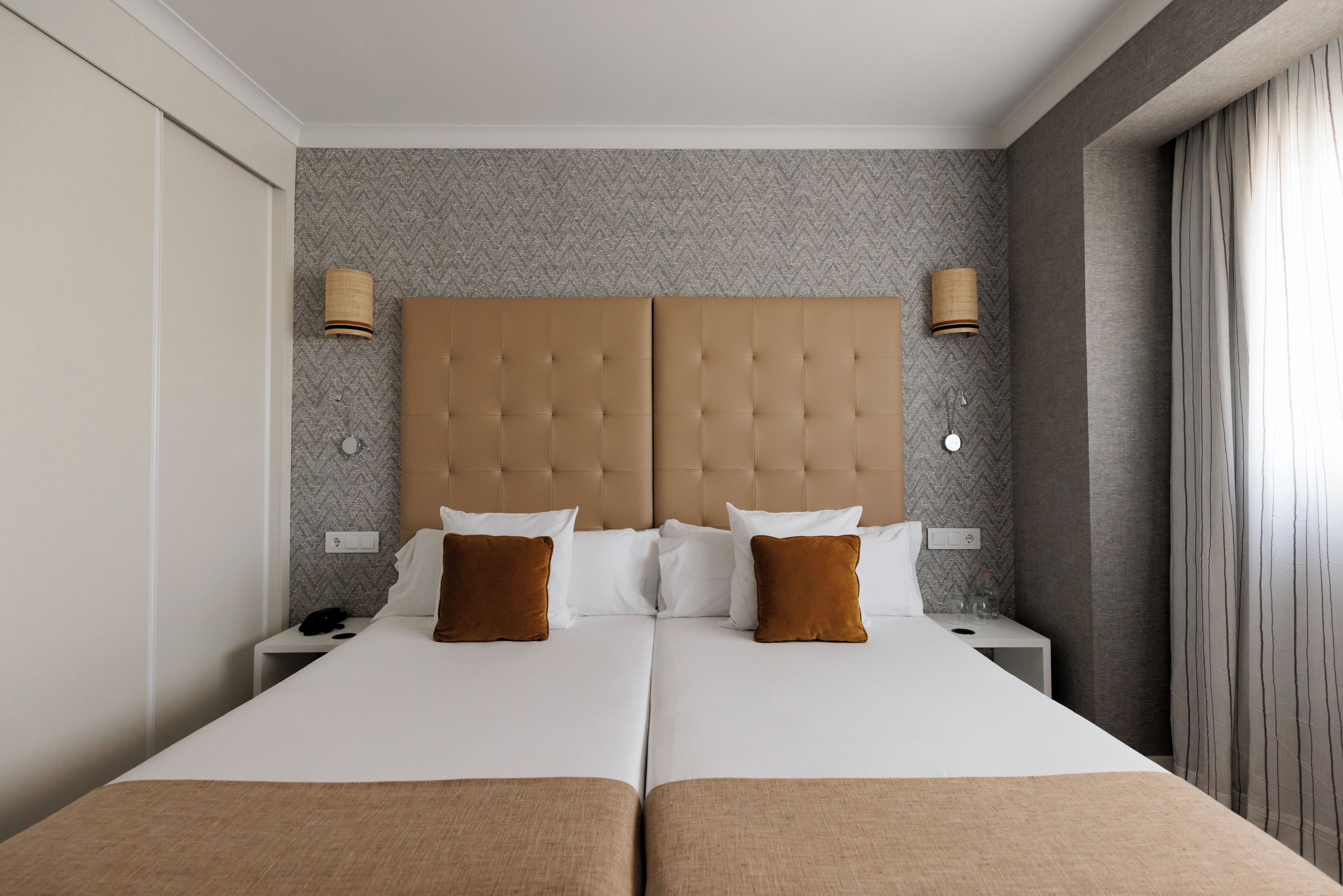 A double bed with a tufted headboard, two bedside tables with lamps, and a herringbone-patterned wall.