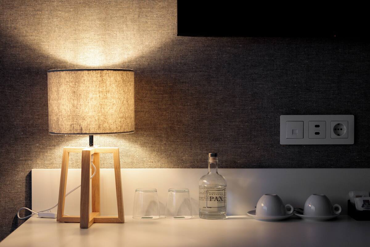 Een nachtkastje met een lamp, een fles PAX, twee glaasjes en twee theekopjes.