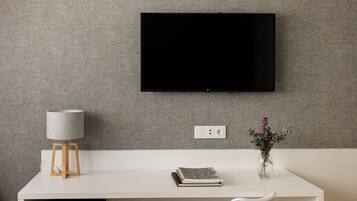 A modern room with a white desk, a mounted TV, a lamp, a vase with flowers, and a book.