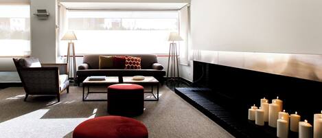 A modern living room with a sofa, armchairs, a coffee table, and a fireplace with candles.