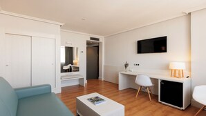 Een moderne hotelkamer met een bank, een bureau, een televisie en een kleine kitchenette.