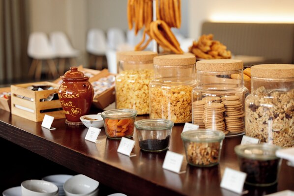 Un bufé con diversos alimentos y recipientes, incluyendo botes de granola, galletas y frutas secas.